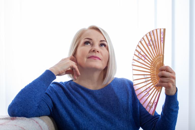 Exploring Homeopathy for Perimenopause Symptoms Woman fanning her face with a delicate fan.