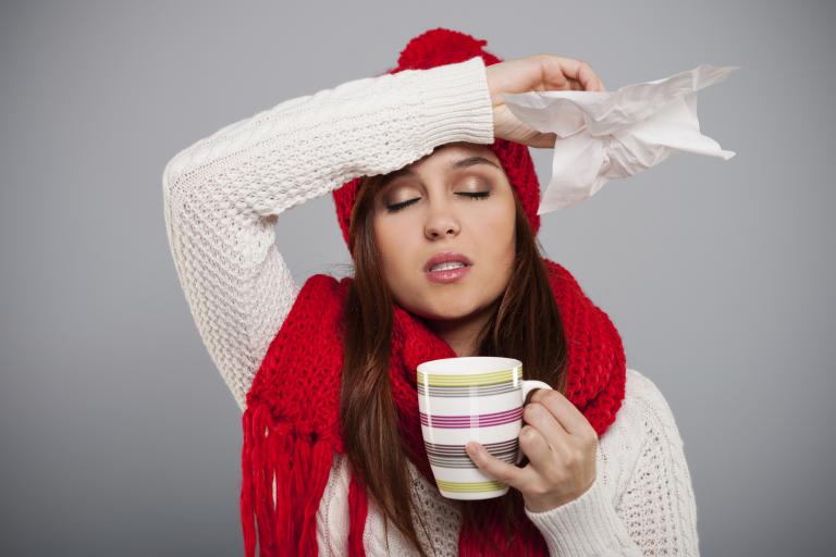 Surviving Cold and Flu Season woman in a hat and scarf with a tissue in her hand drinking tea
